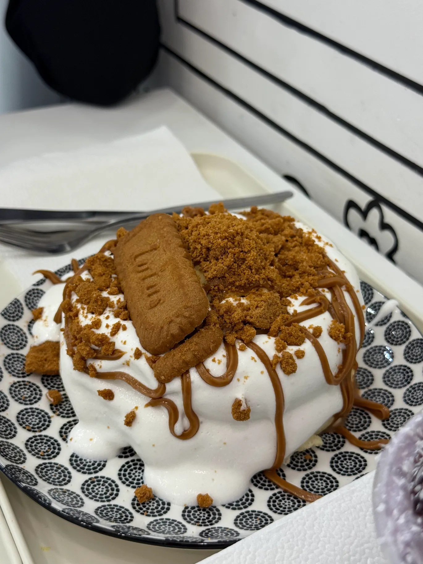 Lotus Biscoff soufflé pancakes topped with milk foam, biscoff sauce, crumbs and a Lotus biscuit, served on a patterned plate at 2D Café Beloved