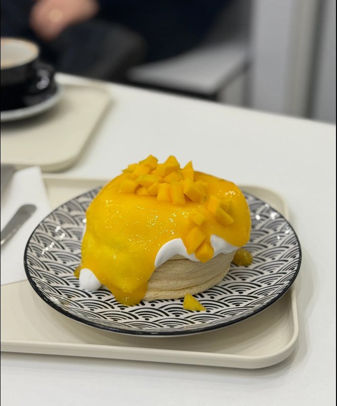 Mango soufflé pancakes with mango purée, fresh diced mango and cream on a patterned plate