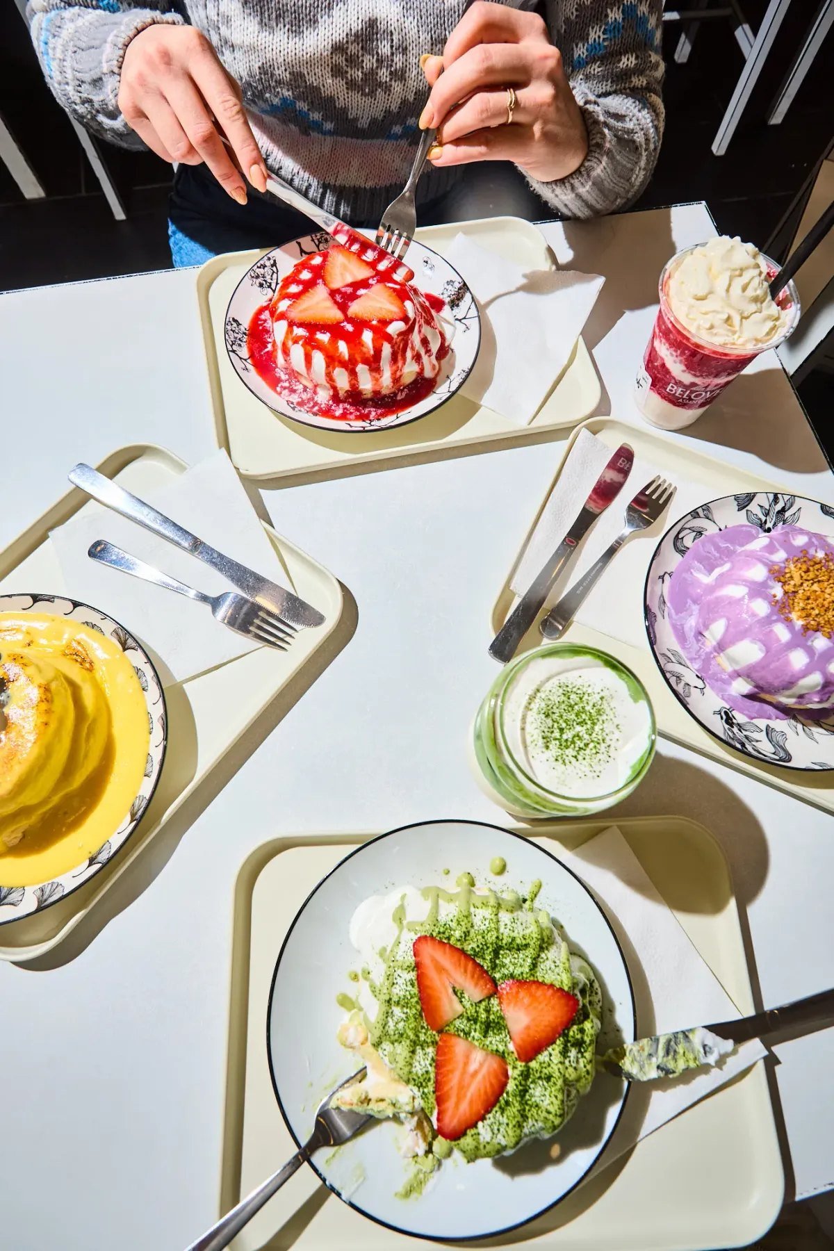 Overhead view of a table at 2D Café Beloved with strawberry, taro and matcha soufflé pancakes, mango pancakes and a matcha latte